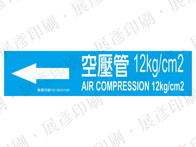 藍底白字，左側箭頭，文字「空壓管 12kg/cm2 AIR COMPRESSION 12kg/cm2」。用途：空壓管路標示流向。語系：繁中/英文